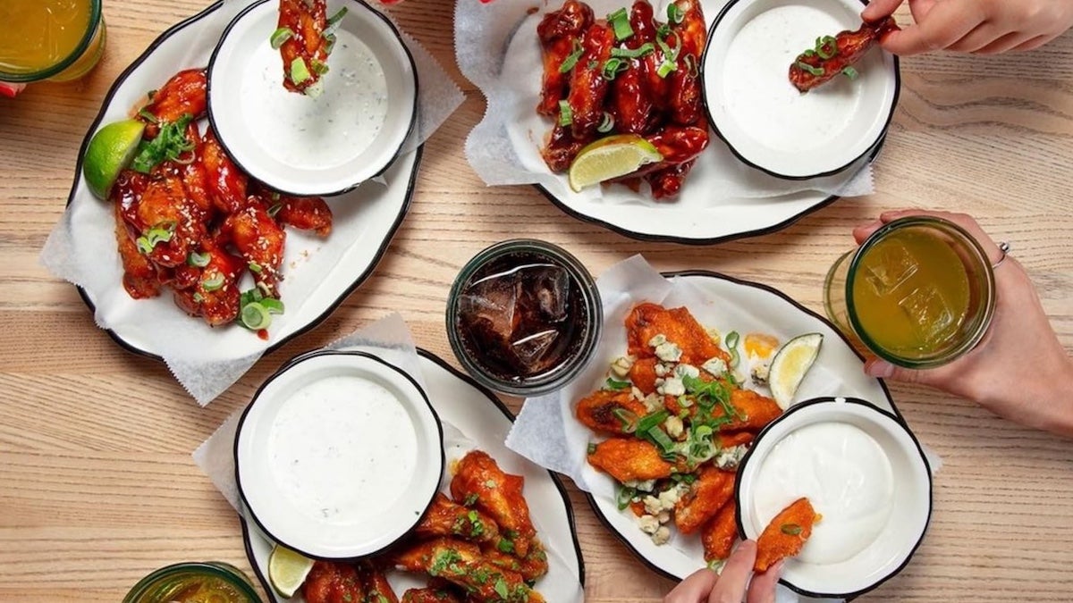 Several plates with chicken wings on them and ranch drip with hands eating